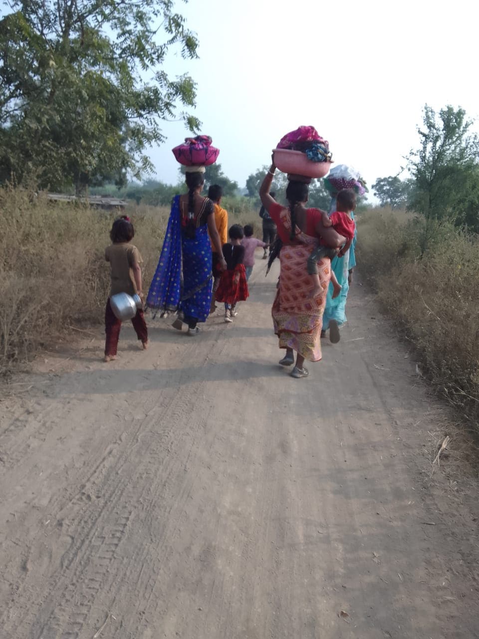 Women and children walking a dirt road carrying their belongings between harvests
